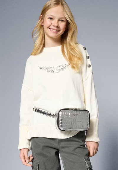 White oversized sweater with wing embroidery, button accents on sleeves, paired with a silver crocodile-patterned belt bag and gray pants.