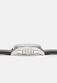 Reloj de acero inoxidable plateado con correa de goma negra, esfera redonda, dos pulsadores y bisel texturizado para un mejor agarre.