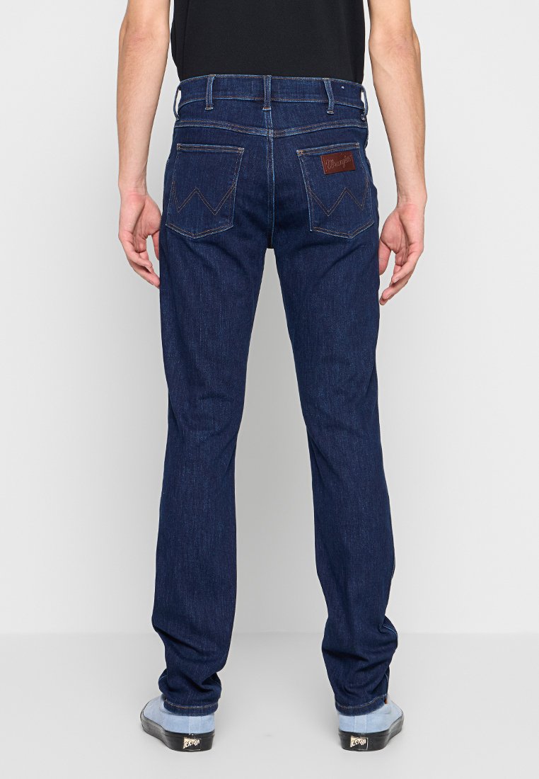 Dunkelblaue Denim-Jeans mit geradem Bein. Merkmale sind sichtbare Nähte, zwei Gesäßtaschen und ein Lederschild mit Markenlogo.