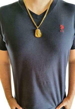 Schwarzes V-Ausschnitt-T-Shirt mit rotem Logo auf der linken Seite, kombiniert mit einer dicken goldenen Kettenhalskette, die einen Löwenanhänger trägt.