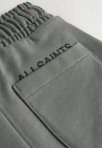 Grå cargoshorts med elastisk midja, har en ficka med klaff och texten "ALLSAINTS" i svart på baksidan. Slät tygtextur.