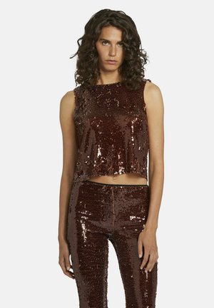 Vrouw met krullend haar die een mouwloos donkerbruin pailletten crop top en bijpassende hoge pailletten broek draagt.