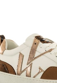 Witte sneaker met bruine suède accenten, gestructureerde bronzen details en een glanzend logo. Beschikt over een glad oppervlak en vlakke zool.