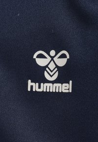 Tela azul marina con un logo blanco de una abeja estilizada con un diseño abstracto y el nombre de la marca "hummel" debajo en letras minúsculas.