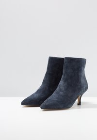 Botines de ante en azul marino oscuro, punta puntiaguda, tacón delgado, textura suave, con cremallera lateral para fácil uso.