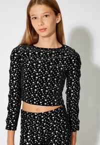 Sort fløjl langærmet crop top med sølv stjerne mønster, med rund halsudskæring og tætsiddende silhuet. Glat tekstur og strækbart stof.