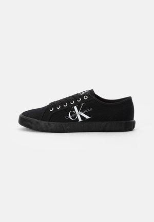 Zapatilla deportiva baja de lona negra con suela de goma negra y logo blanco de Calvin Klein Jeans en el lateral y en la lengüeta.