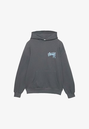 Sweatshirt à capuche gris en tissu doux, comportant une poche avant et un logo brodé bleu sur la partie gauche de la poitrine.