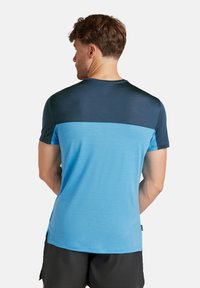 Kortärmad t-shirt med blå kropp och marinblå övre panel. Tillverkad av lätt material, med rund hals och sidoklipp för rörelsefrihet.