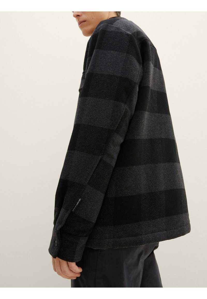 Schwarz-graue kariert Jacke aus dickem Stoff, mit lockerer Passform, Knopfmanschetten und einem Etikett-Detail am Ärmel.