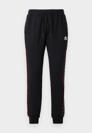 Schwarze Jogginghose mit elastischem Bund, roten Seitenstreifen und Kappa-Logo. Hergestellt aus glattem Stoff, mit gerippten Bündchen und einem lockeren Schnitt.