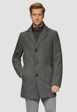 Grau karierten Übermantel mit abgerundetem Kragen, drei schwarzen Knöpfen und Seitentaschen, über einer schwarzen gesteppte Innenjacke getragen.