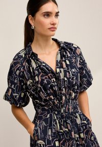 Rochie bleumarin cu mâneci pufoase scurte, având un model abstract de peisaj urban în culori pastelate. Talie elastică și buzunare laterale.