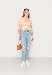 Top cropped floral laranja com mangas bufantes, jeans claros desfiados, ténis brancos de plataforma e uma bolsa laranja com corrente.