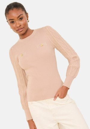 Béžový žebrovaný svetr s kabelovým vzorem na nafouklých rukávech, zdobený dvěma zlatými knoflíky vpředu. Hladká textura, přiléhavý střih a bezproblémový výstřih.