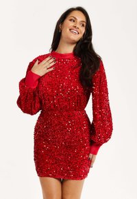 Red sequined dress with long puff sleeves, cinched waist, and soft texture. Features a high neckline and a fitted silhouette.