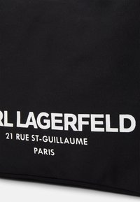 Černá látková taška s výrazným bílým nápisem „CARL LAGERFELD“ a adresou „21 RUE ST-GUILLAUME PARIS“ pod ním.