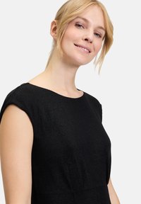 Schwarzes Kleid mit einem glatten, strukturierten Stoff, kurzen Ärmeln und einem runden Ausschnitt, der auf der Oberfläche einen subtilen Glanz zeigt.