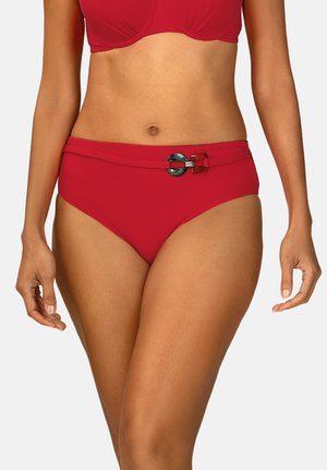 Kobieta w czerwonym dwuczęściowym stroju kąpielowym z ozdobnym paskiem z okrągłymi i prostokątnymi klamrami na dolnej części.