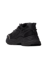 Zapatilla deportiva negra hecha de malla y material sintético, con una suela gruesa y texturizada y una lengüeta en el talón, con acentos sutiles.