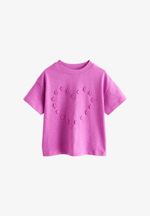 Różowy t-shirt z krótkim rękawem i okrągłym dekoltem oraz małymi wypukłymi kształtami kwiatów ułożonymi z przodu w kształt serca.