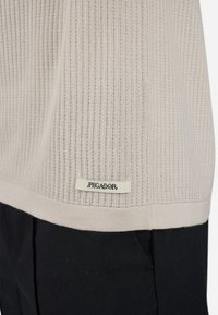Lys beige ribbet striktrøje med en kontrasterende sort bund. Har et mærke med "PEGADOR" broderet på en cremefarvet etiket i kanten.
