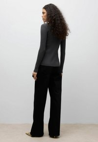 Šedý vypasovaný svetr v kombinaci s černými širokými kalhotami. Svetr má dlouhé rukávy a ribovaný vzor. Outfit doplňují špičaté baleríny.