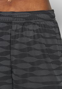 Svarta sportshorts med ett texturerat mönster av vågiga linjer i olika nyanser av grått. Har en elastisk midjeband för komfort.