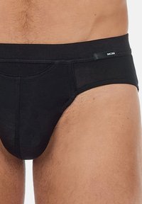 Schwarze Unterhose aus glattem Stoff, mit einer figurschmeichelnden Passform, niedrig geschnittenem Bund und einem kleinen Logo-Akzent an der Seite.