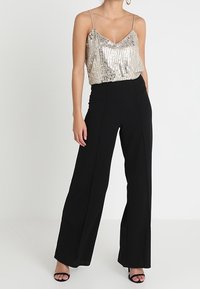 Pärlbeströdd guldtop med tunna band, i kombination med högmidjade svarta vida byxor och öppetåiga svarta sandaler.