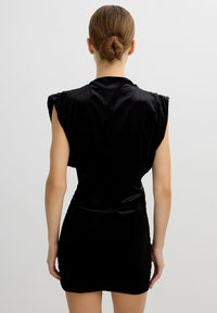 Vestido mini negro con mangas cortas, textura de terciopelo suave, silueta ajustada y sutil detalle de encaje en los laterales.