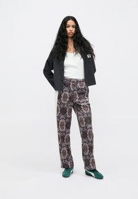 Σκούρο γκρι υφασμάτινο cardigan πάνω από ένα λευκό tank top, συνδυασμένο με μοτίβο μωβ παντελόνι που έχει κόκκινες και μαύρες λεπτομέρειες και πράσινα αθλητικά παπούτσια.