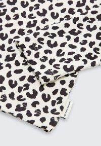 Leopardmönstrad tyg i svart och vitt. Texturerad yta med ribbat mönster. Kanten har stickade detaljer och en etikett.