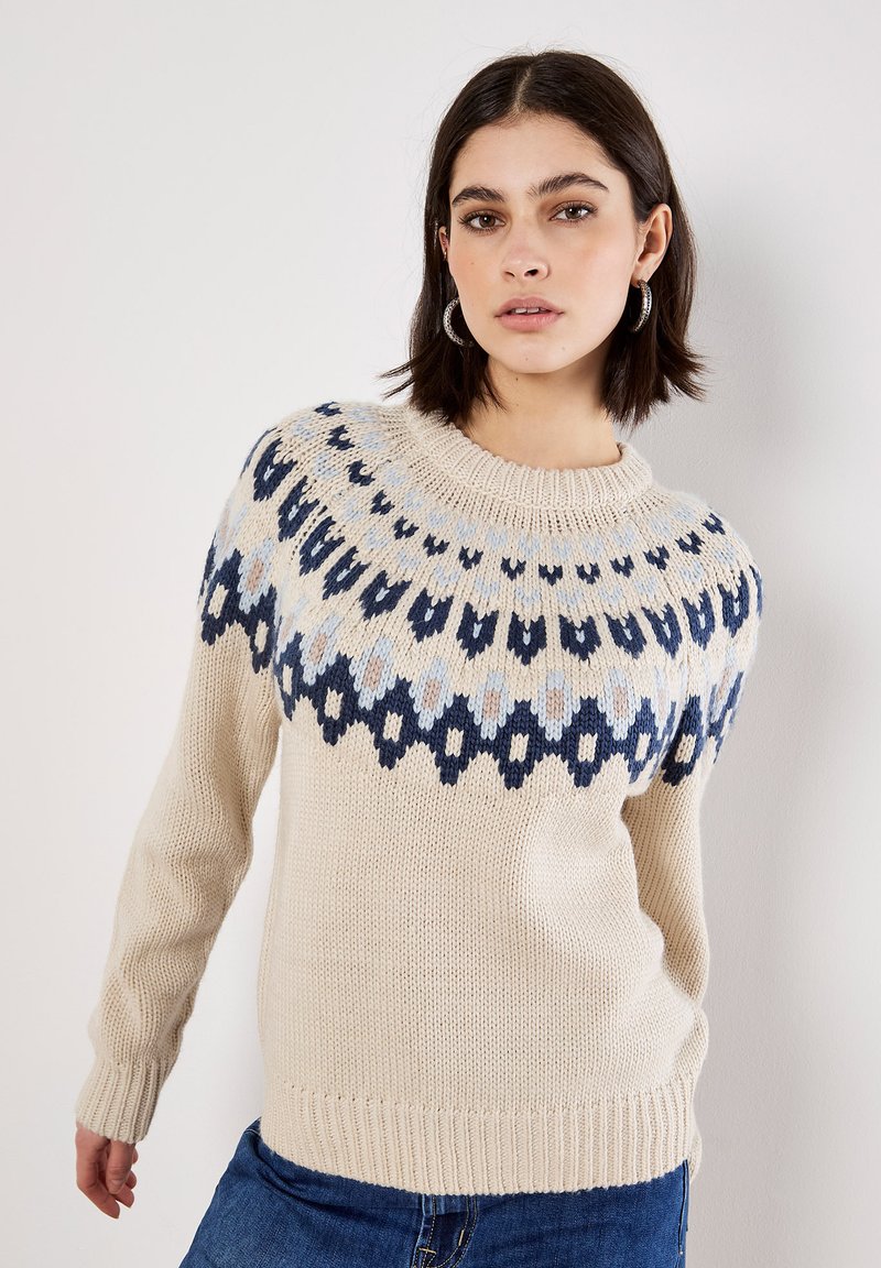 Suéter de punto beige con cuello redondo, que presenta un patrón geométrico azul y azul claro alrededor de los hombros y puños acanalados.