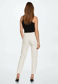 Pantalons beiges taille haute au design fuselé, en tissu texturé, avec poches arrière et couture contrastée. Associés à un haut noir et des talons.