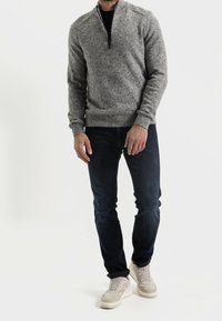 Grauer gestrickter Pullover mit einem Reißverschlusskragen, kombiniert mit dunkelblauen Jeans und hellgrauen Sneakers. Der Pullover verfügt über einen strukturierten Stoff.