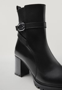 Zwart lederen enkelboot met een zilveren gesp en een stevige blokhak met profielzool.