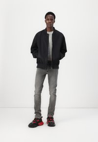Chaqueta bomber negra, suéter gris acanalado, jeans grises y zapatillas negras con acentos rojos. Diseño simple, corte recto, textura suave.