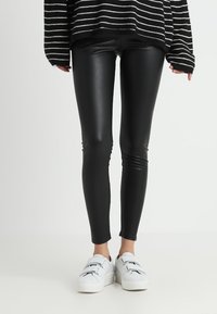 Svarta imitation läderleggings med en slät textur, figurnära design, matchade med vita sneakers med justerbara remmar.