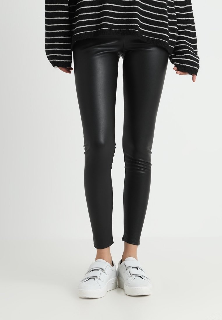 Svarta imitation läderleggings med en slät textur, figurnära design, matchade med vita sneakers med justerbara remmar.