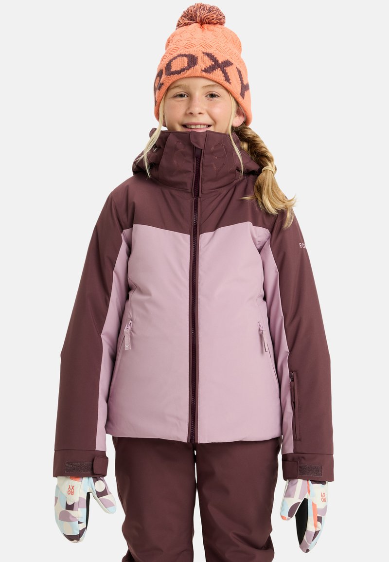 Paarse en kastanjebruine skijas met een capuchon, ritssluiting en twee voorzakken. Gedragen met gemusterde handschoenen en een heldere oranje gebreide muts.