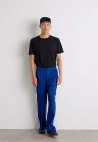 Camiseta de algodón negra y pantalones deportivos azules con acentos laterales en azul claro. Los pantalones cuentan con una cinturilla elástica y un corte recto.
