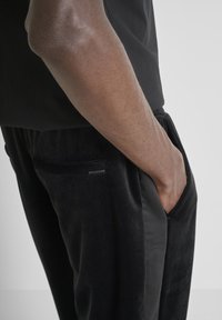 Zwarte joggerbroek van zacht, gestructureerd materiaal. Voorzien van zijzakken en een subtiel logotag. Gemaakt met een elastische tailleband voor een aangesloten pasvorm.