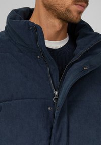 Dunkelblaue steppjacke mit hohem Kragen, Reißverschluss und Druckknöpfen. Strukturierter Stoff mit gerippten Details auf der Innenlage.