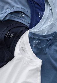 Kuus T-särki erinevates sinise, valge ja tumesinise toonides. Kõigil on ümara kaelusega disain ja "NEXT" silt taga.