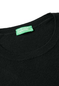 Czarny sweter z okrągłym dekoltem, dzianinową fakturą i zieloną metką z napisem "UNITED COLORS OF BENETTON" przymocowaną do kołnierza.