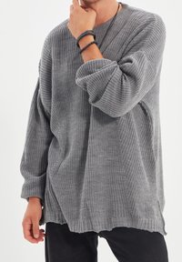 Pull gris en maille avec une coupe ample, un motif texturé, des épaules tombantes et un ourlet côtelé. Stylisé avec un pantalon foncé et des accessoires.