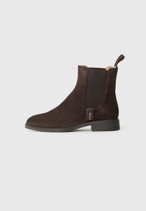 Brown suede ankle boot with elastic side panels and a pull tab. Features a rounded toe and a low stacked heel. Gold branding detail present.