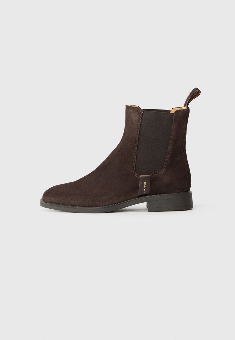 Bottine en daim marron avec panneaux élastiques sur les côtés et une languette. Dispose d'un bout arrondi et d'un petit talon empilé. Détail de marque doré présent.
