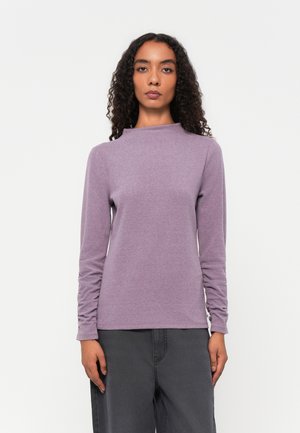 Tæt siddende langærmet top i blødt lilla stof, med en mock neck og ruchærede ærmer for ekstra tekstur og detaljer.
